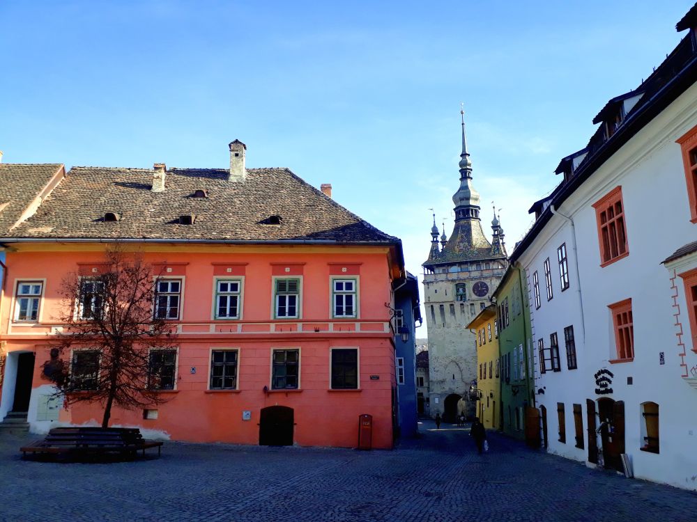 A square with pretty pastel-colored buildings and, seen down a street, an ornate tower.
