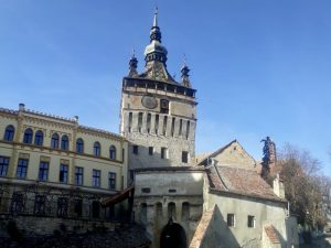 Large building with a tall square tower in its center with a clock and a pointed roof.