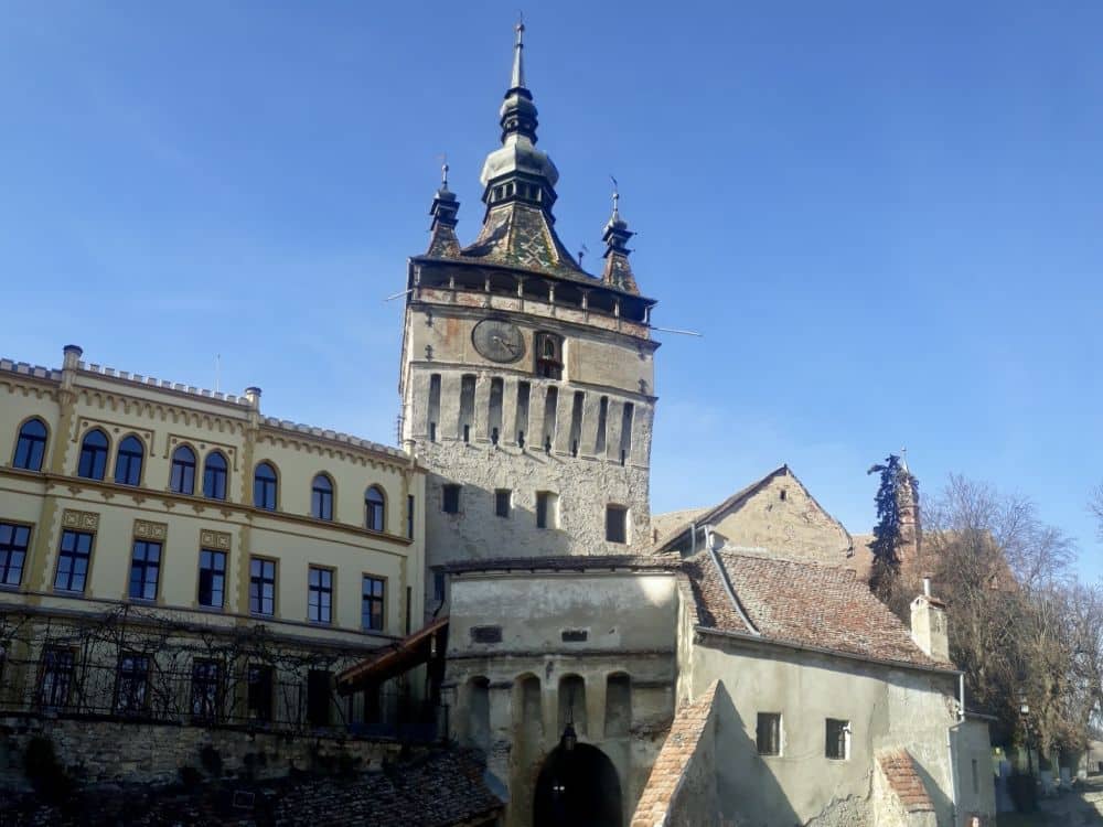 Large building with a tall square tower in its center with a clock and a pointed roof.
