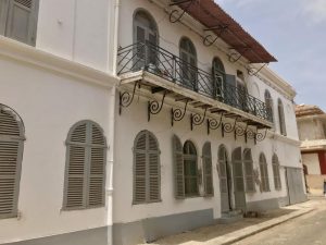 A white building of 2 stories with arched shuttered windows and a balcony.