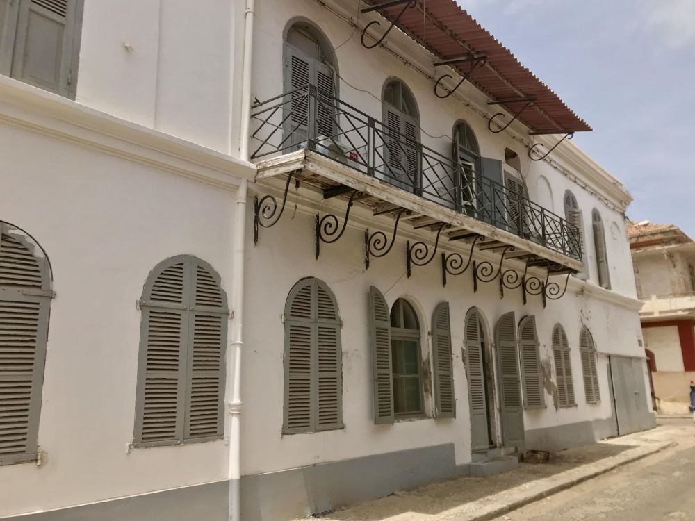 A white building of 2 stories with arched shuttered windows and a balcony.