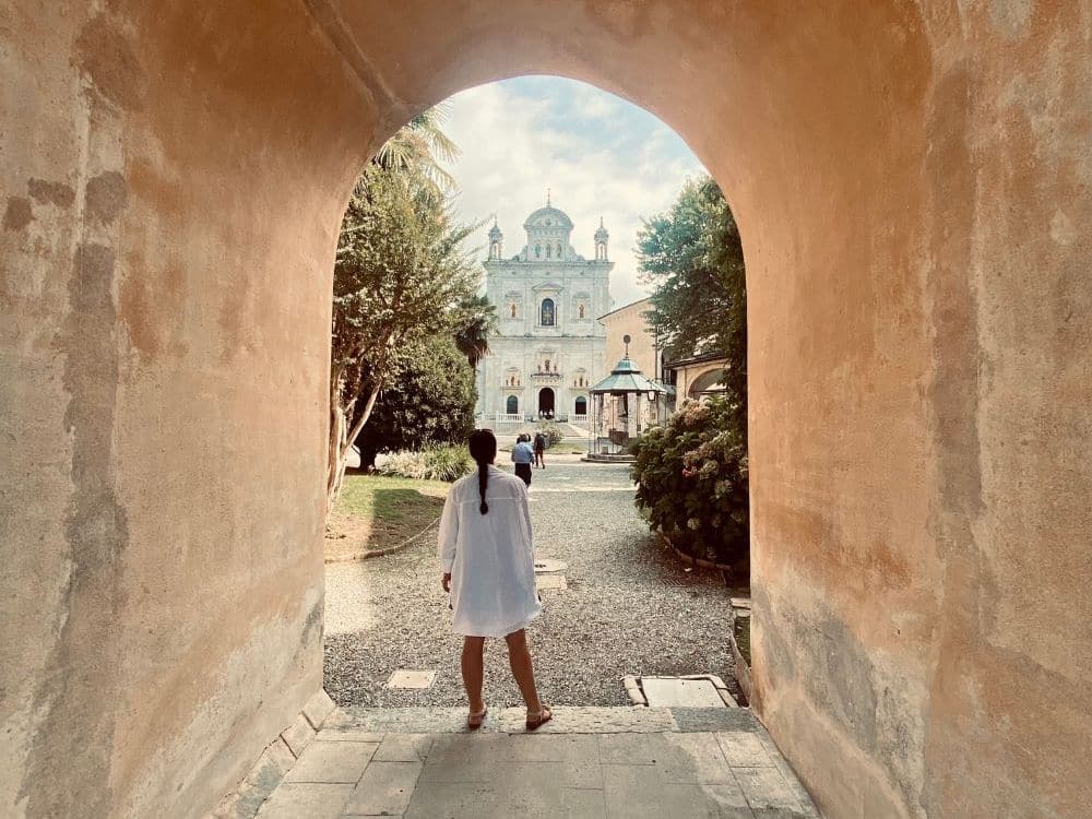 An archway with white walls, a person standing with her back to the camera, and beyond her, an open space with a church directly opposite, framed in the archway.
