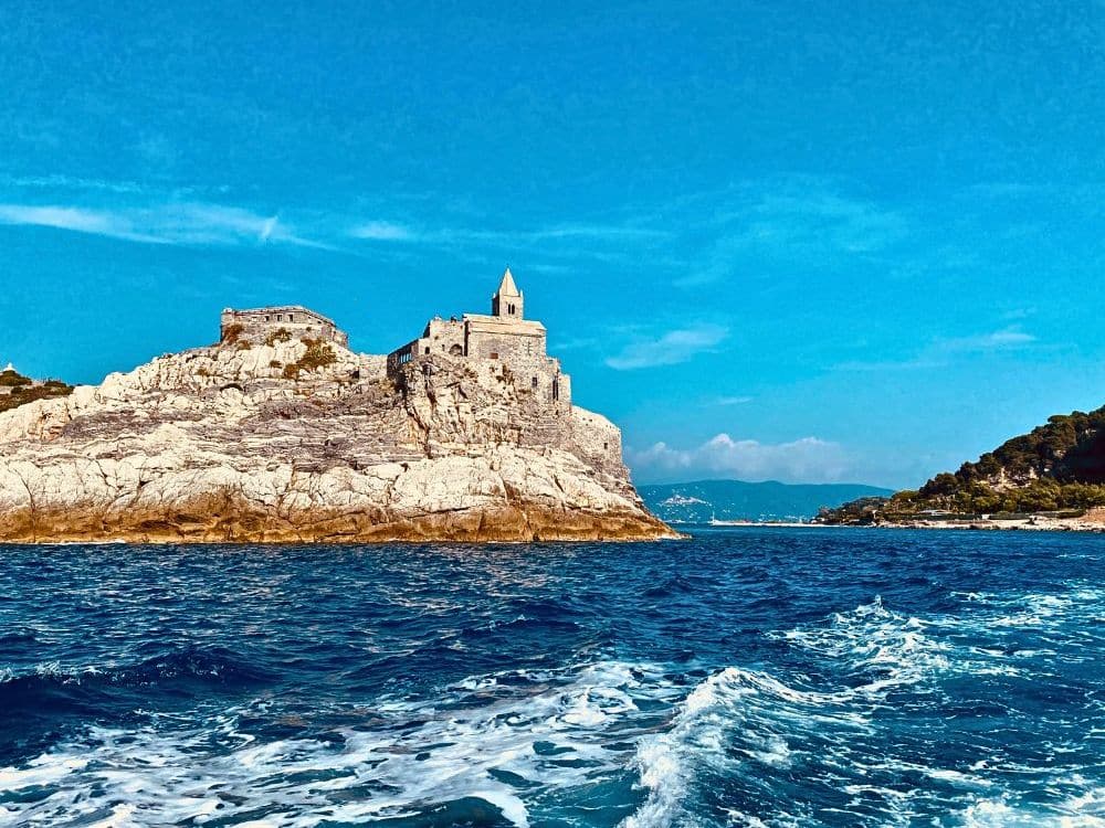 As seen from the water at a distance, a high cliff down to the water with a stone church perched on top.