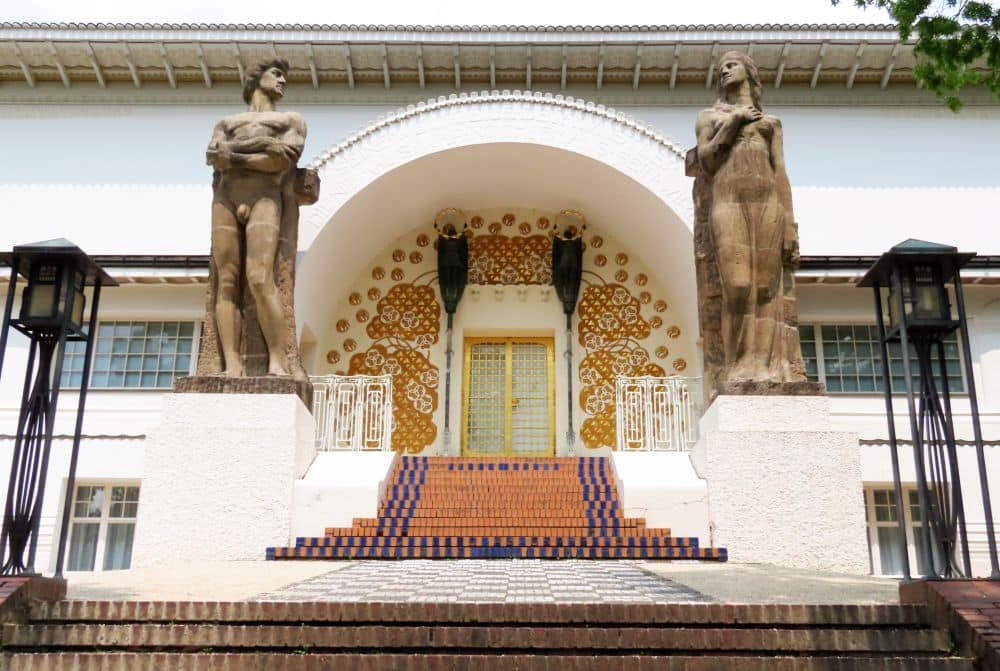 An arched doorway with mosaics inside it and two statues flanking it.
