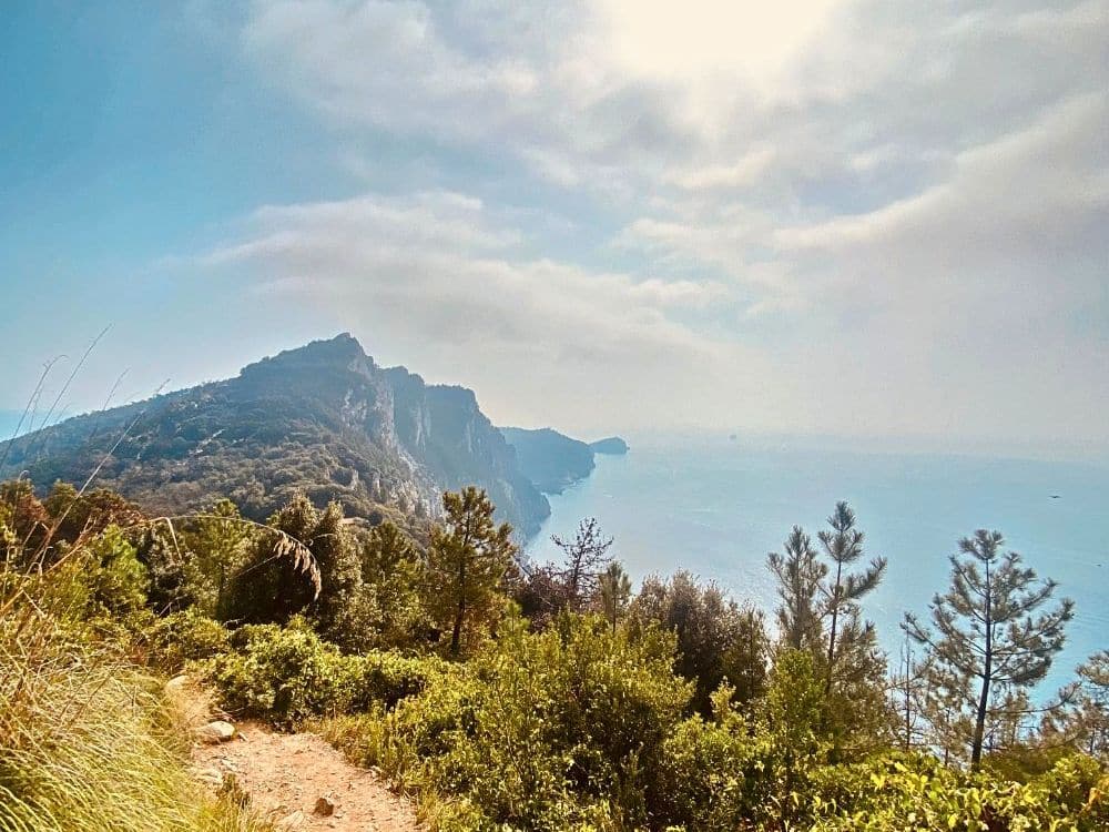 A bit of dirt trail along a cliff, with a dramatic cliff-edged coastline ahead.
