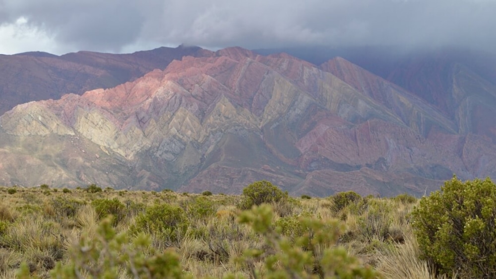 A view from a hill toward a multicolored mountain in the distance.