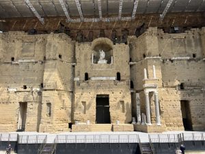 A closer view shows the theater backdrop with a statue at its center, and pillared elements on either side.
