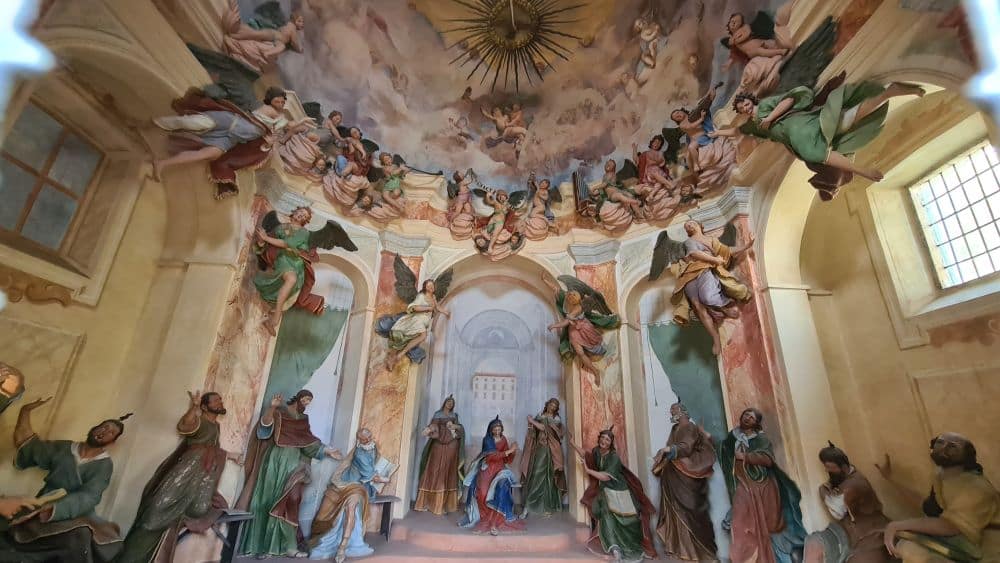 Mary at the center, lots of humans and angels as statues on the ground, or the walls, plus more figures painted on the walls.