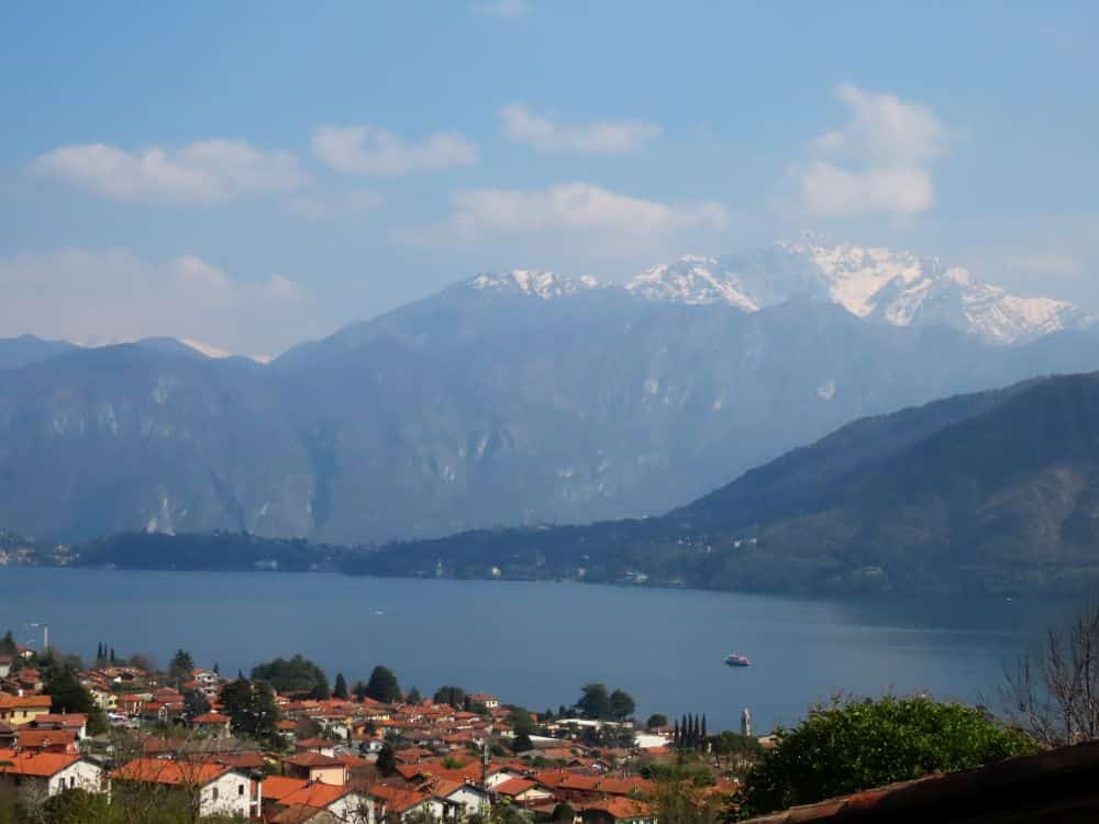 Roofs of a town below on the edge of a lake. Tall mountains beyond the lake with snow caps.