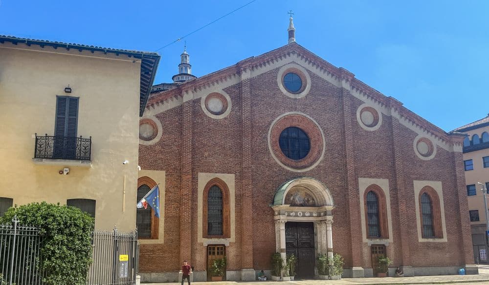 A flat brick facade with a decorative arched doorway in the center, a round window above that, and arched windows on either side of the doorway.