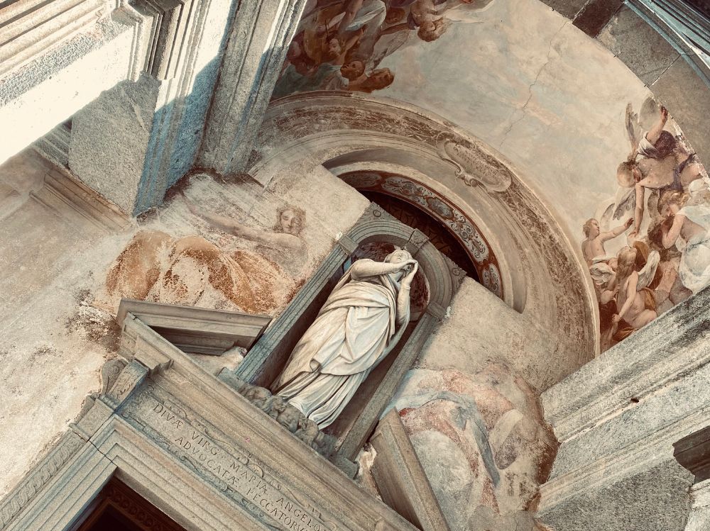 A statue in a niche above a large doorway, with frescos of angels and saints painted around it.