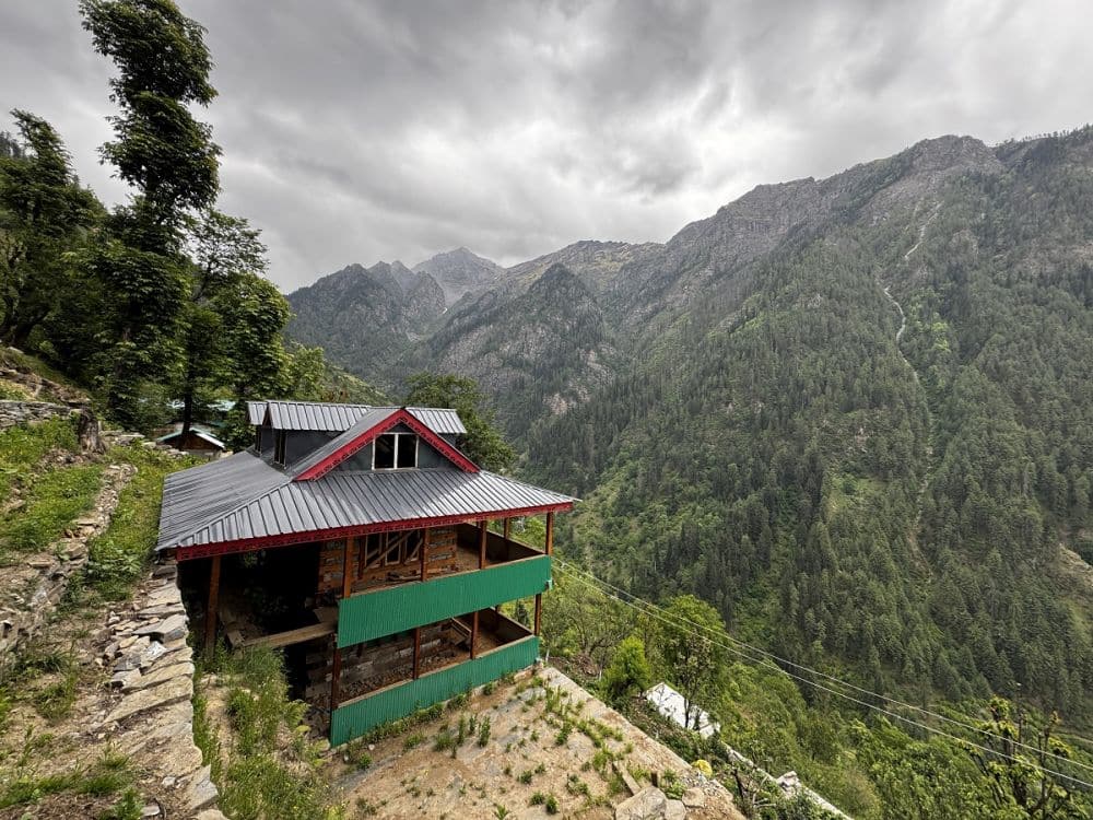 A chalet-like house on the side of a hill with a big view of a valley and a mountain range behind it.