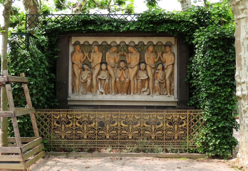 A bas-relief shows a row of people, some standing and, between them, some sitting.