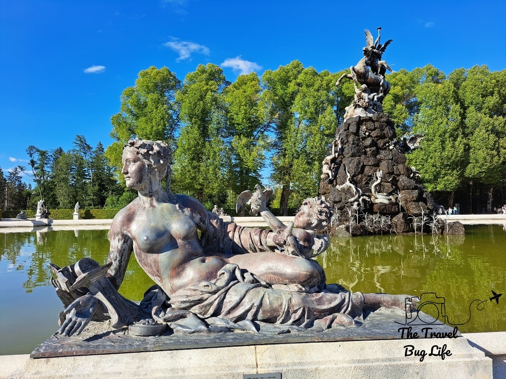 An ornate statue in a classical style next to a pond, with another ornate statue in the background.