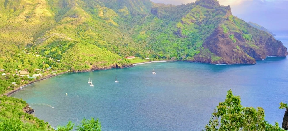 A blue-water bay with a few small boats at anchor, surrounded by lush green hills.