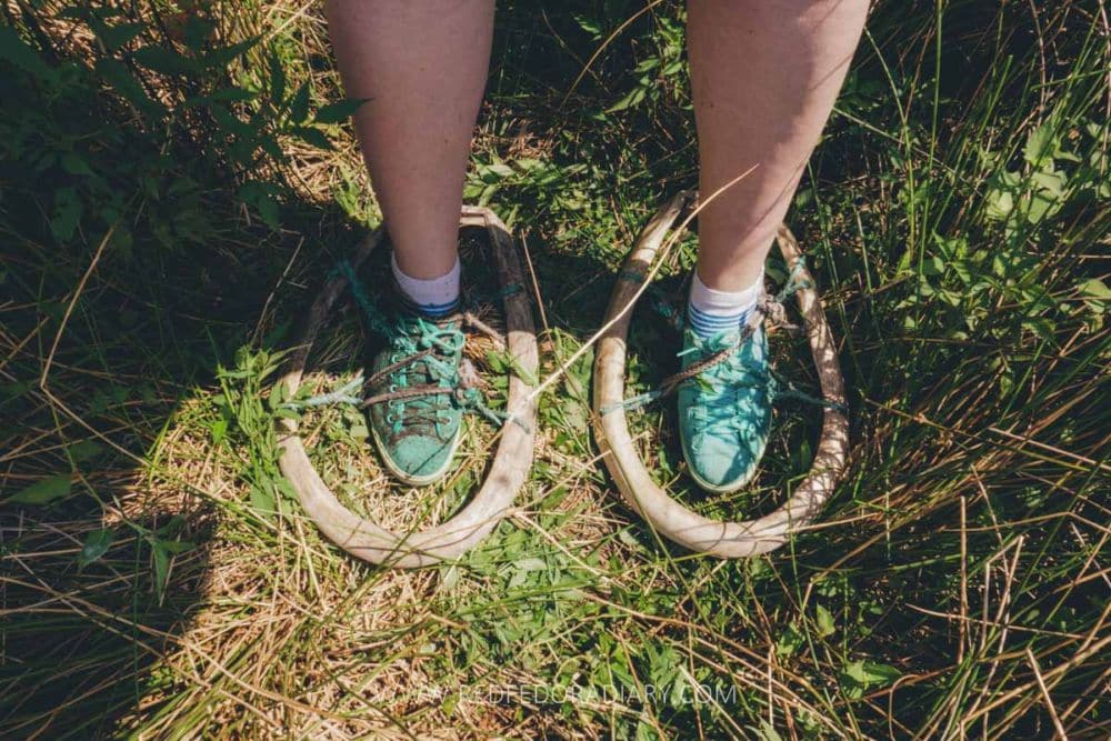 Looking down at a person's feet, with the feet and shoes tied into bog skis, which are much like snowshoes.