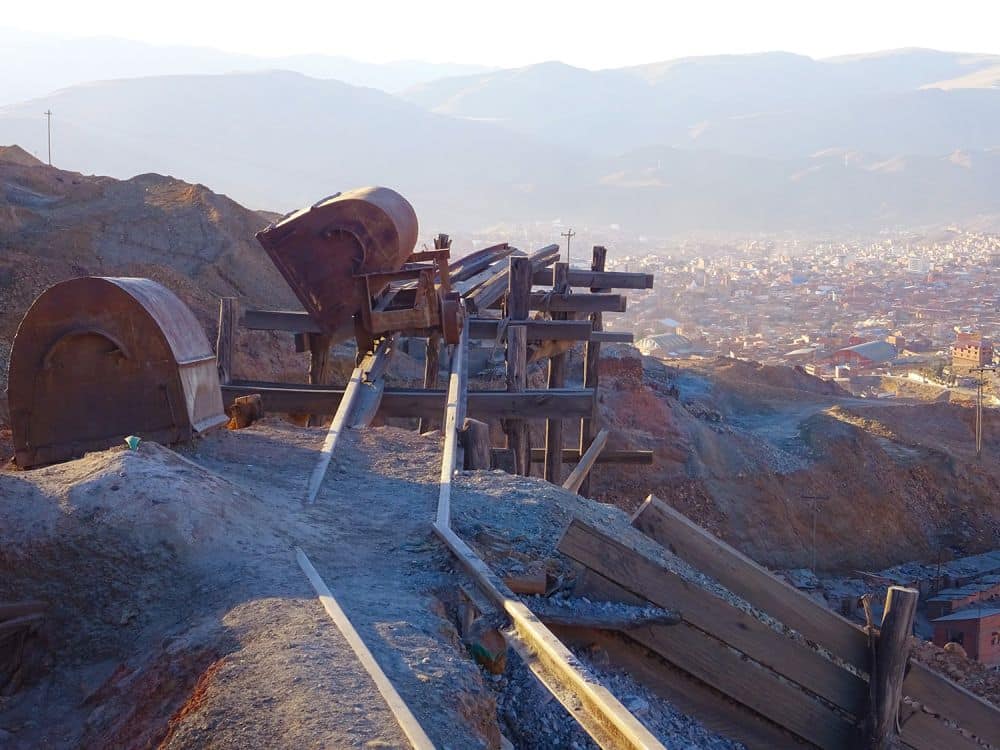 A dirt path, industrial machinery, then a big view to the city below and mountains beyond that.