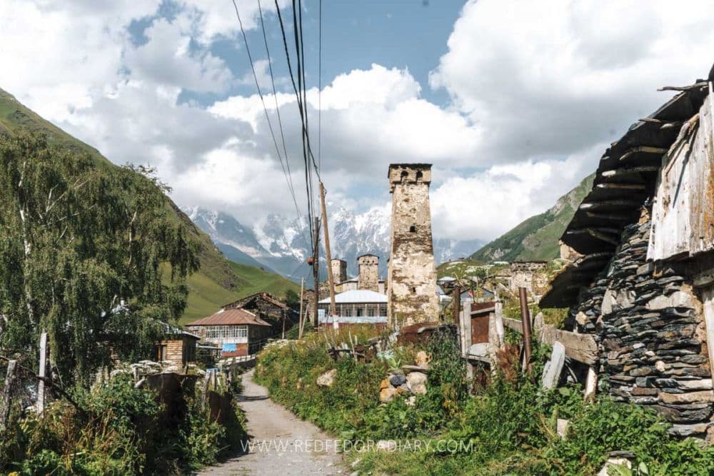 On a narrow dirt road leading into a village, passing a tall stone tower.