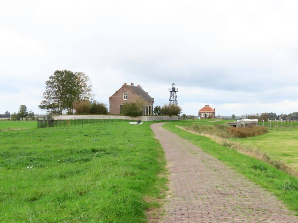 A brick path through green, with a house in the distance and a beacon tower. On the right the land is lower.
