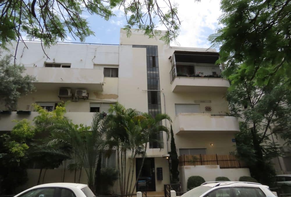 White building, cantilevered balconies left and right, with a vertical glass strip at the stairway above the entrance.