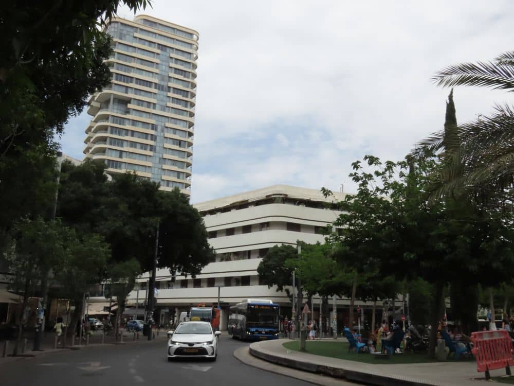 A curve in the street with behind it a large building that is 5-6 stories high and wider than it is high, with long horizontal strips of balcony around both visible sides.