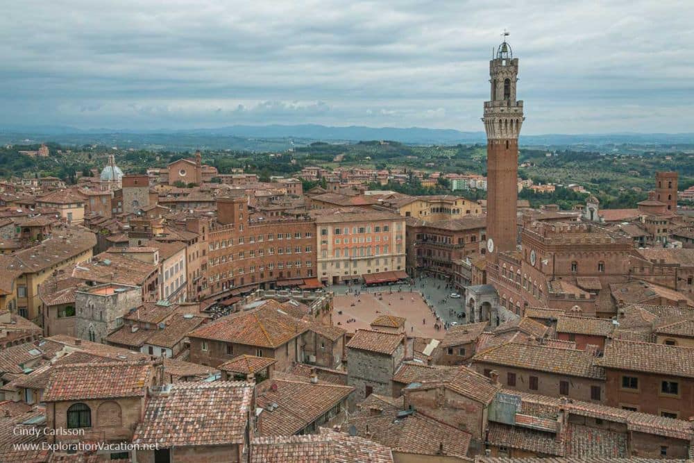 View over the Historic Centre of Siena with the Piazza del Campo in the middle and a tall bell tower.