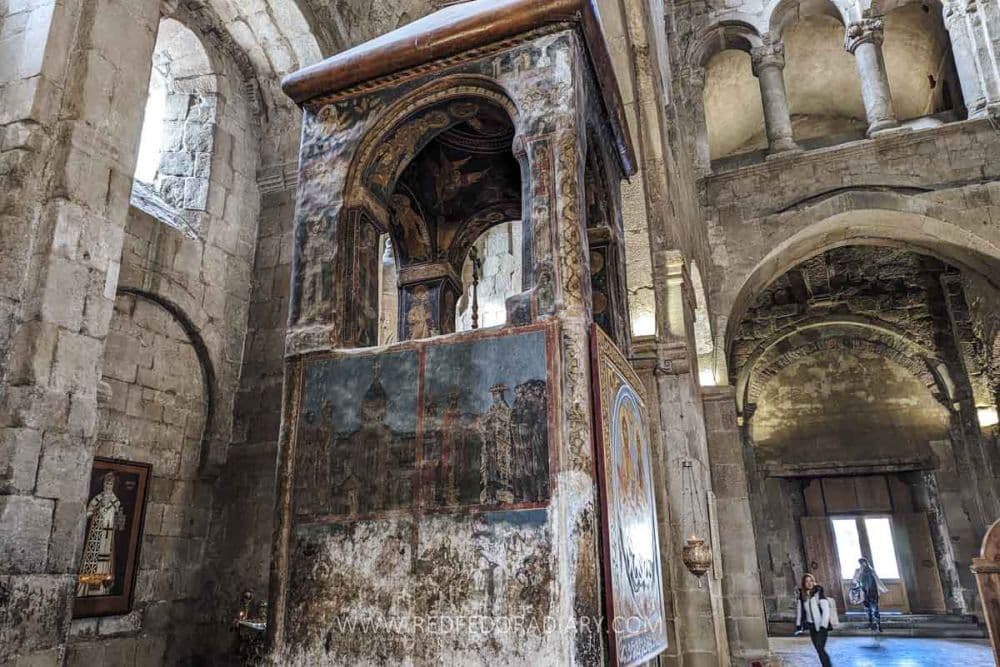 A square pulpit inside the cathedral, topped with 4 columns holding up a small roof. The sides of the pulpit are covered in frescoes.