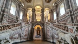 Looking from the top of the central stairway back down, but the two upward staircases, one one each side are visible as well. Walls, bannisters, ceiling are all covered in baroque artwork.