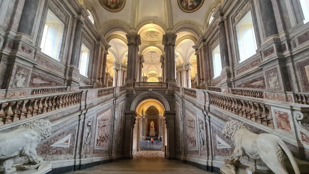 Looking from the top of the central stairway back down, but the two upward staircases, one one each side are visible as well. Walls, bannisters, ceiling are all covered in baroque artwork.