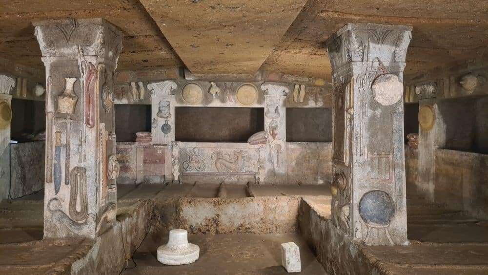 A room filled with human-sized beds carved from rock, two pillars with bas-relief depictions of various tools, some human-sized slots in the back wall, all of it with traces of paint.