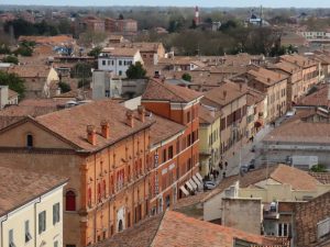 View from above down a wide street in Ferrara, lined with buildings in pastel colors or plain red brick.