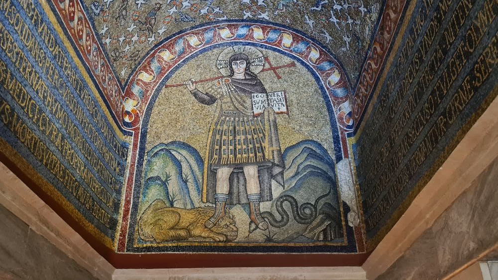A young Jesus, with a halo, holding a cross and a book, stands on a lion with one foot and a snake with the other.