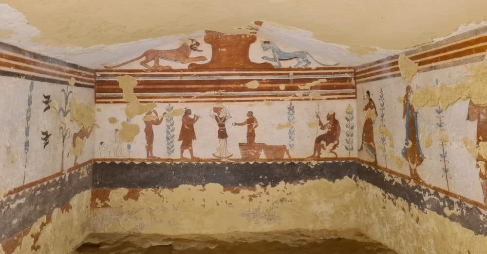 Three walls of a stone room, with a horizontal scene of people engaged in various activities. On the central wall are a red lion and a blue panther.