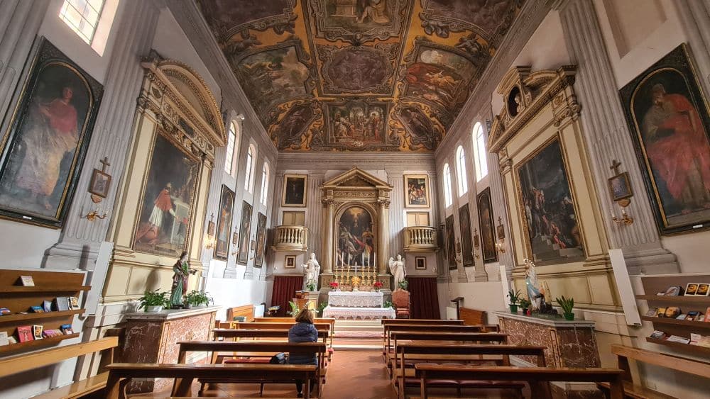 A small church with pews covering the floor, and a very ornate ceiling in Baroque style