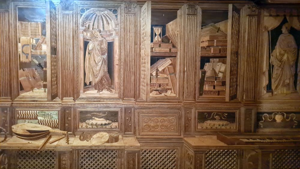 Tromp l'oeil wood inlay images of shelves and cupboards with items on the shelves.