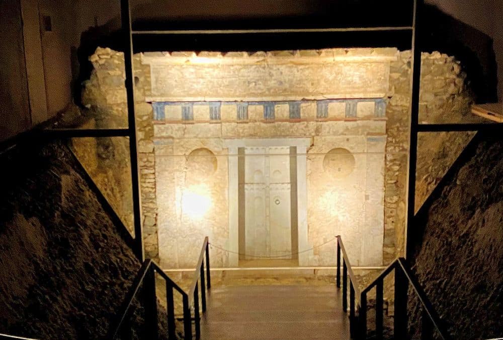Looking down a dark stairway to a wall with some decorative elements carved and painted about its entrance.