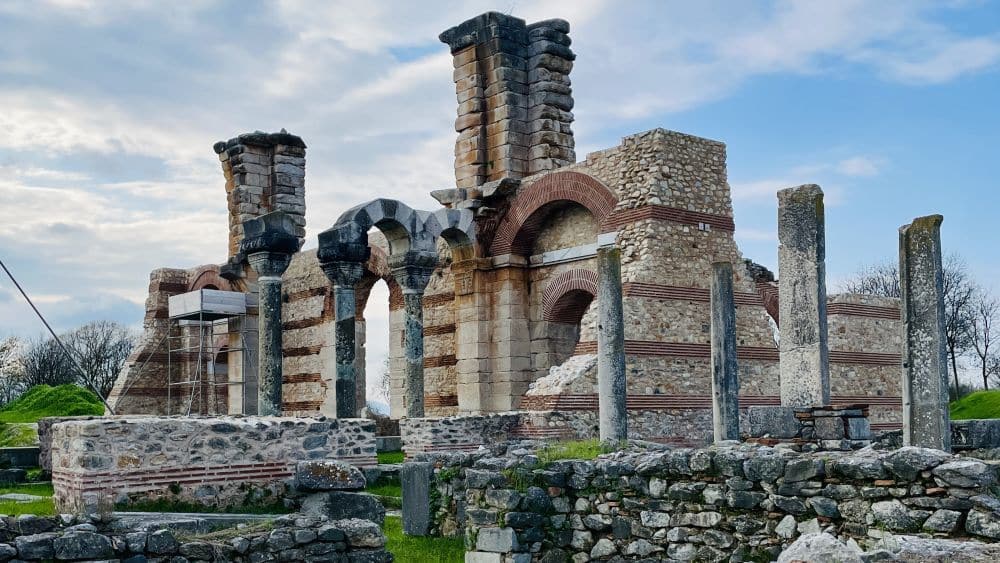 Ruins with some intact arches and pillars, striped in rows of brick and stone.