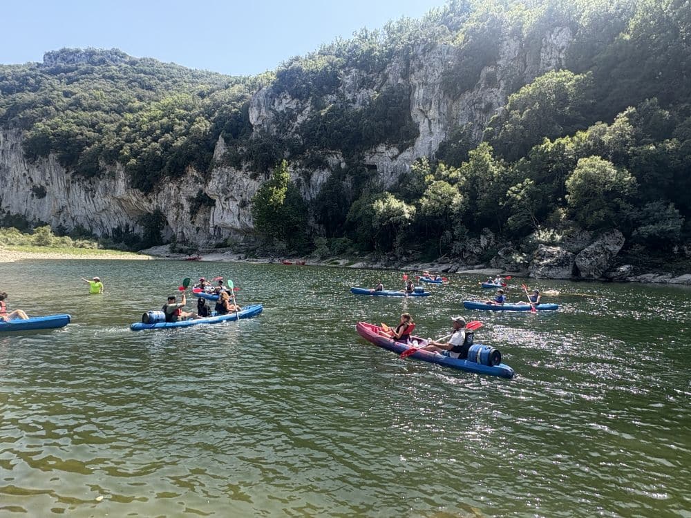 Kayaks on a river beside steep cliffs.