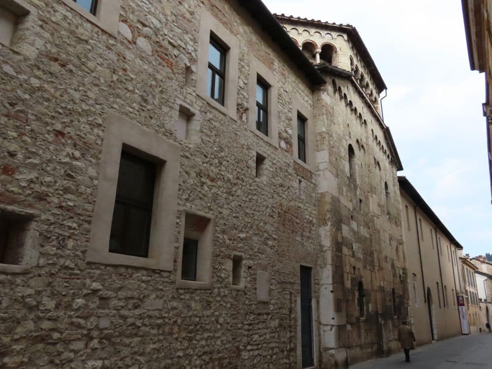 A stone wall along a narrow street is just about 2-3 stories high.