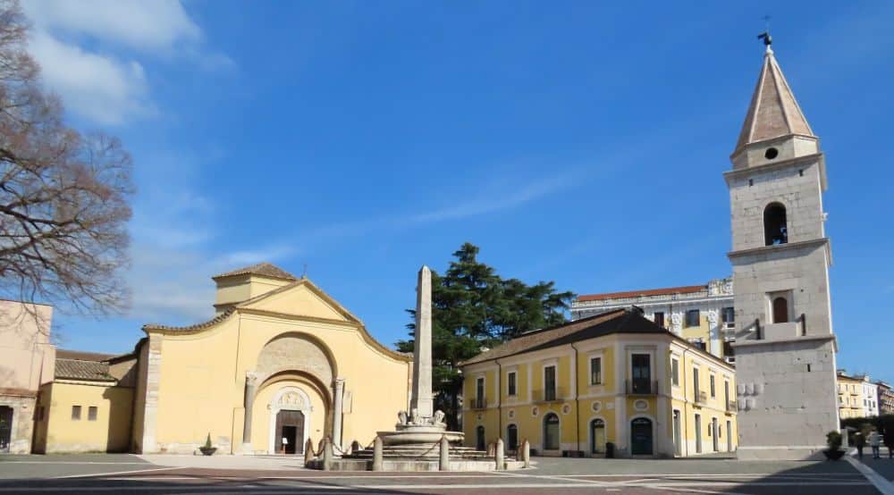 A church on the left with a stuccoed facade rising in a curve to a point. On the right, a free-standing campanile.