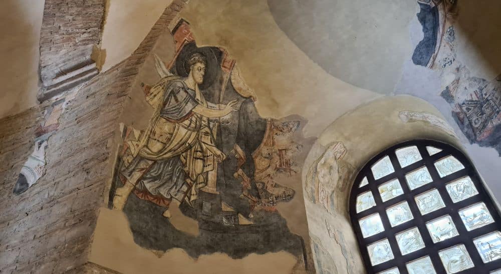 A fresco high on a curved wall shows a man dressed as a knight extending his hand.