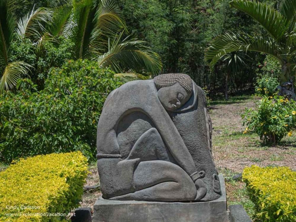 A stone carving of a person kneeling and crouching down, wearing wrist shackles.