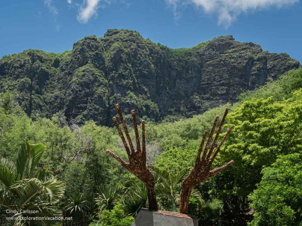 View of the mountain with, in the foreground, a sculpture that looks like elongated hands.
