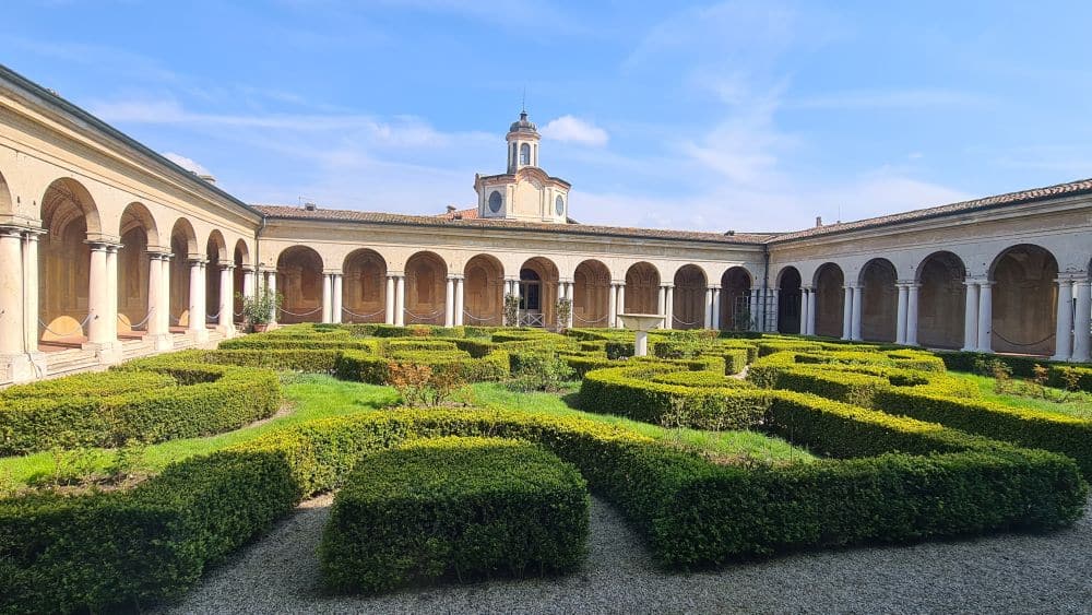 A formal garden of neat hedges surrounded by single-story porticos with arches.