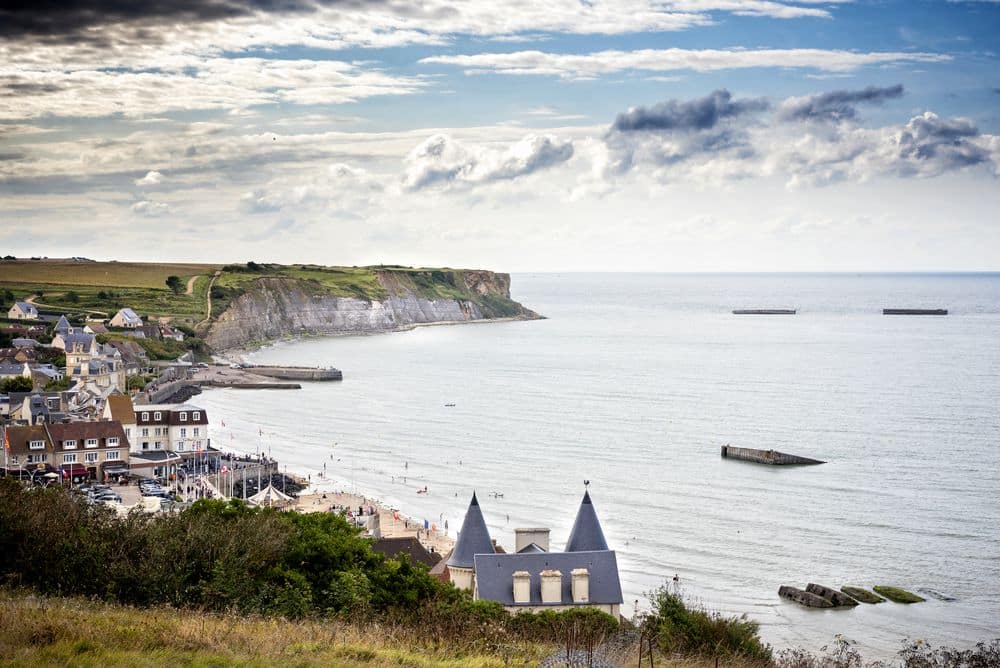 View over a coastline with a town and beyond that, cliffs. Large objects visible in the water.