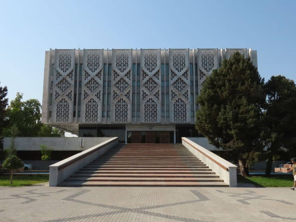 A long gradual staircase leads to a rectangular block of a building with a repeating vertical pattern in the concrete.