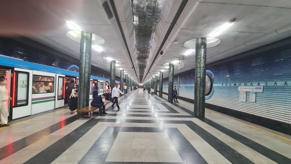 Looking down a long metro platform, blue walls, shiny columns, a train on the left-hand track.