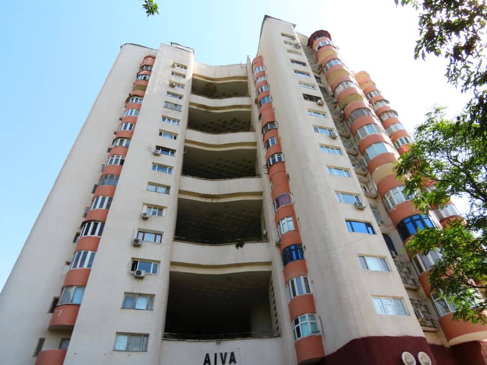 Looking up at a tall apartment building with large openings up the face and on either side, cylindrical verticals extending outwards.